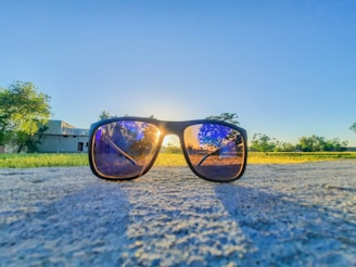 A pair of black sports smart sunglasses resting on a wooden bench with sunlight filtering through trees.