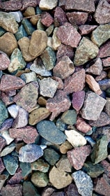 A collection of variously colored stones, ranging from earthy browns and greens to muted purples and blues. The stones vary in size and have rough, irregular shapes.