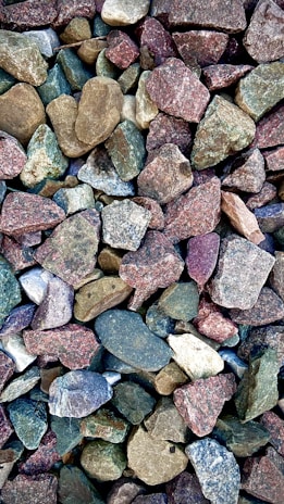 A collection of variously colored stones, ranging from earthy browns and greens to muted purples and blues. The stones vary in size and have rough, irregular shapes.