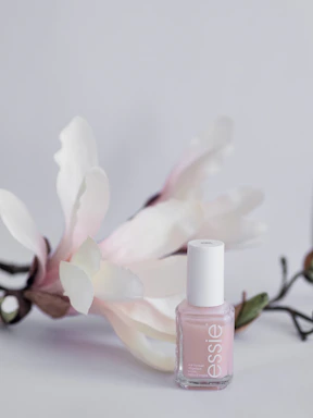 Elegant blush pink nail polish bottle with rose gold cap on a soft marble surface.