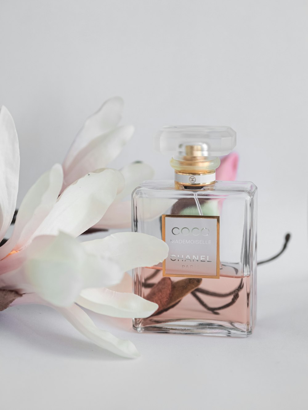 white and pink flower beside perfume bottle