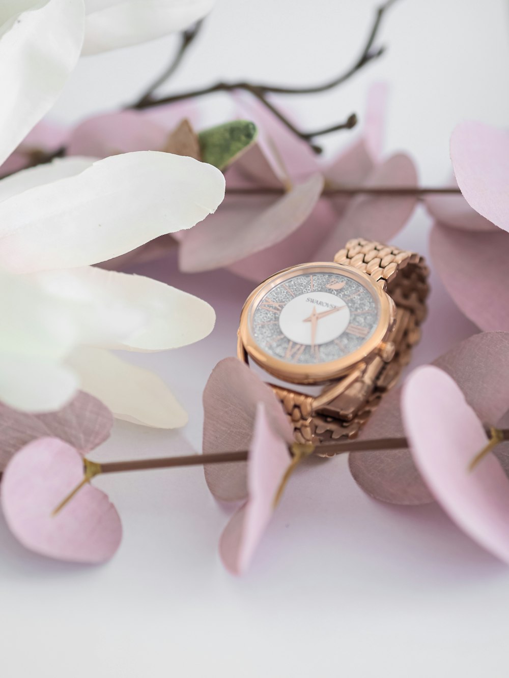 gold and white analog watch on white flower