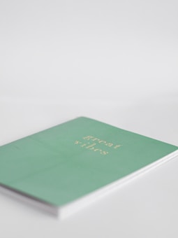 A minimalist notebook with a pastel green cover featuring the phrase 'great vibes' in gold lettering, placed on a simple white background.