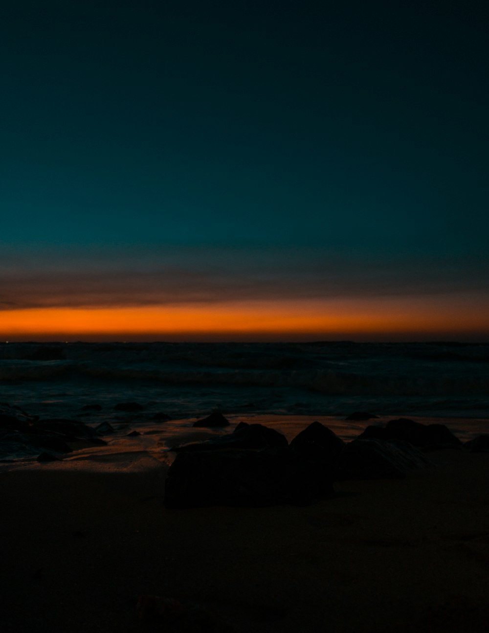 silhouette of rocks on seashore during sunset