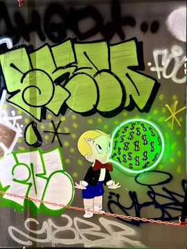 A cartoon character with blonde hair and a red bow tie is depicted blowing a bubble filled with dollar signs. The background features vibrant graffiti art in shades of green, black, and white with abstract shapes and lettering.