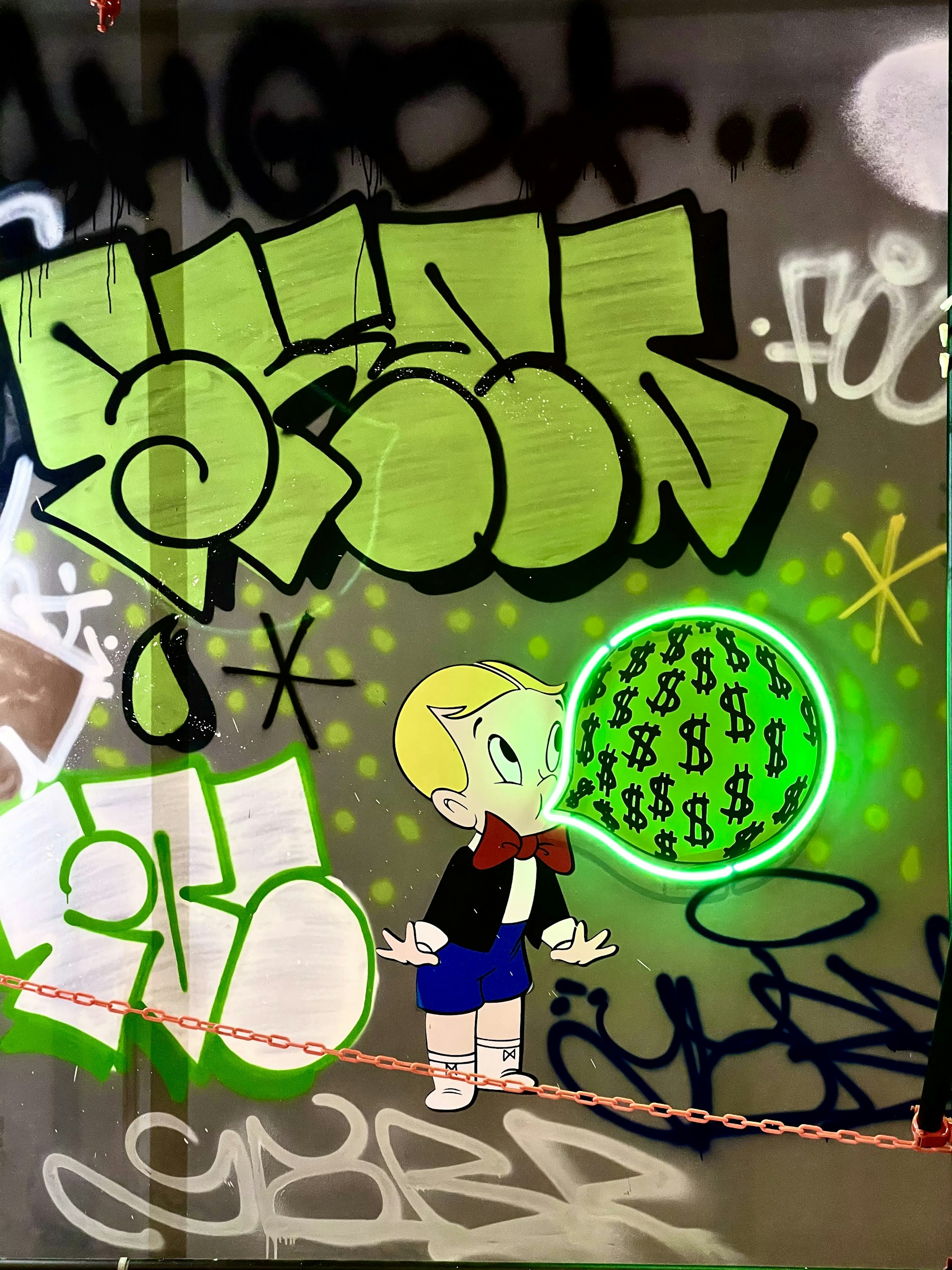 A cartoon character with blonde hair and a red bow tie is depicted blowing a bubble filled with dollar signs. The background features vibrant graffiti art in shades of green, black, and white with abstract shapes and lettering.