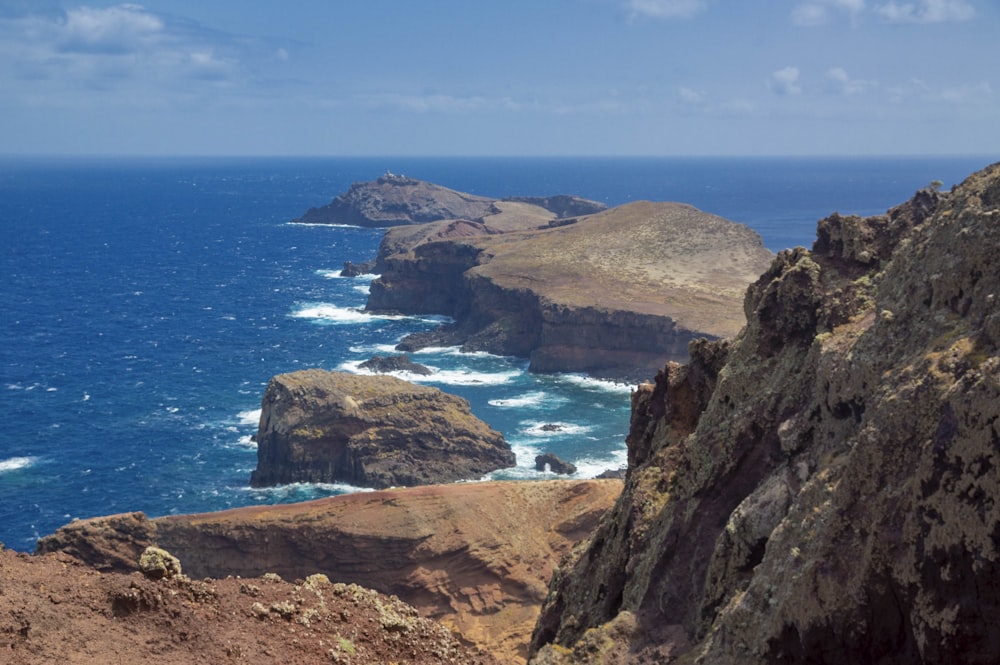 brown rocky mountain beside blue sea under blue sky during daytime