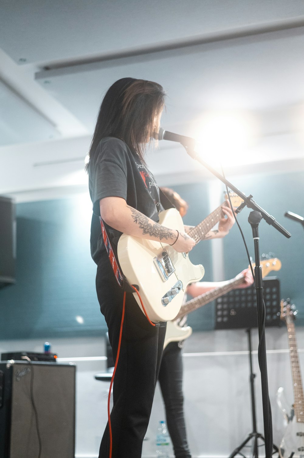 mulher na camiseta preta que joga a guitarra elétrica branca e marrom stratocaster
