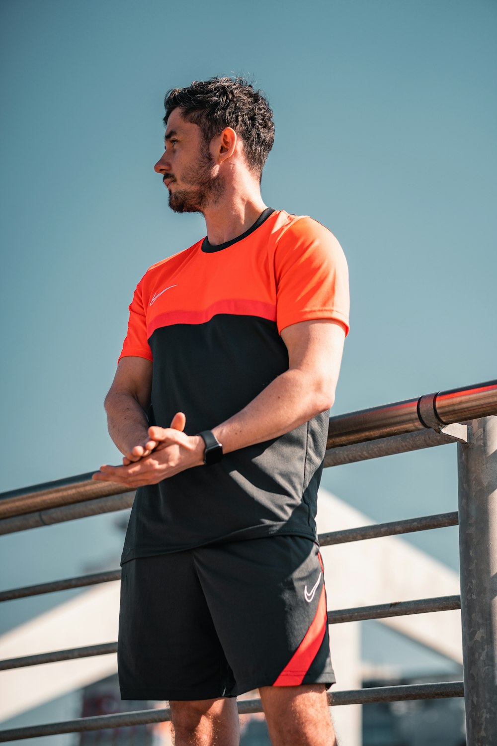 man in orange crew neck t-shirt and black pants standing on balcony during daytime
