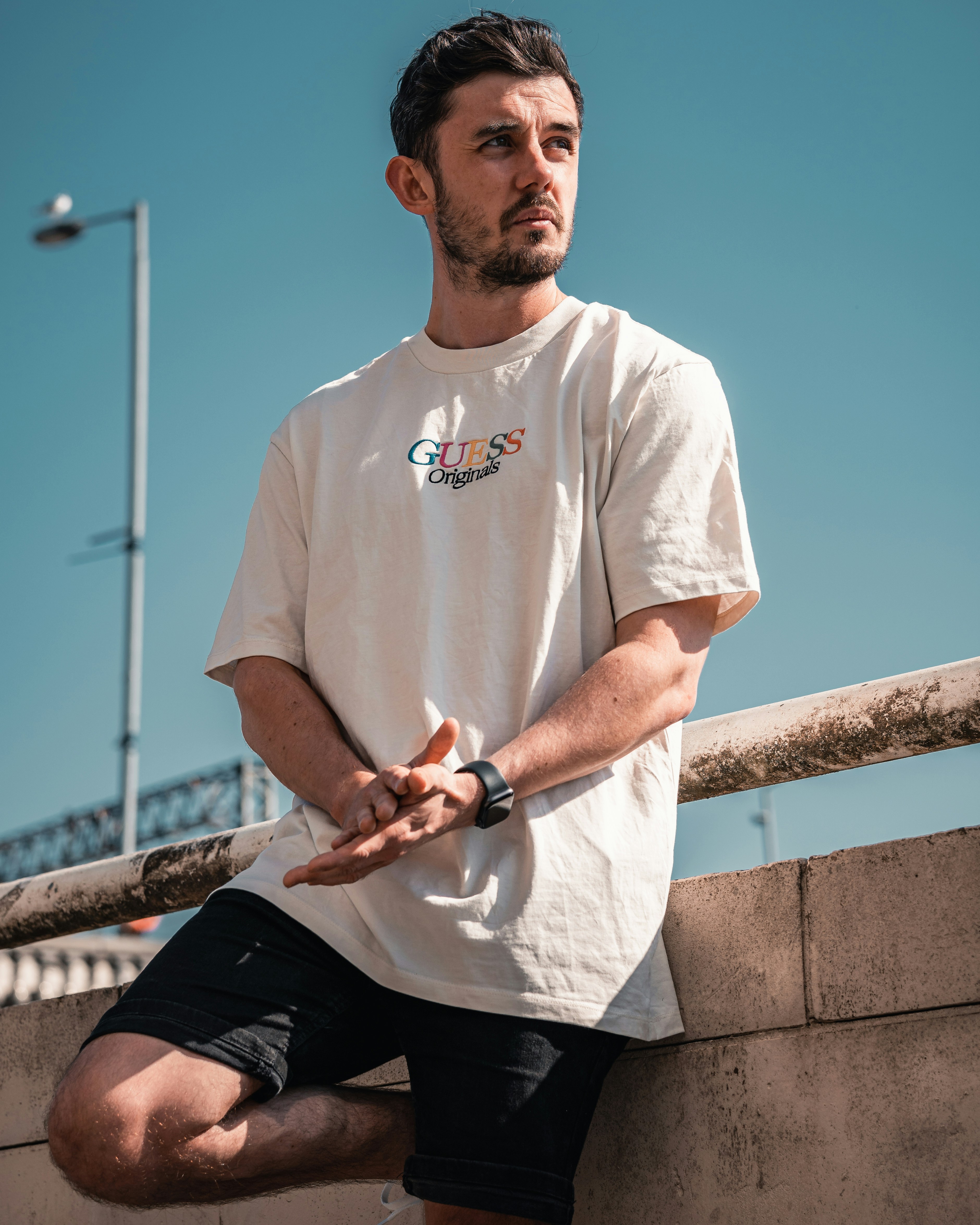 man in white crew neck t-shirt and black pants sitting on brown wooden fence during