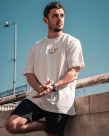 man in white crew neck t-shirt and black pants sitting on brown wooden fence during