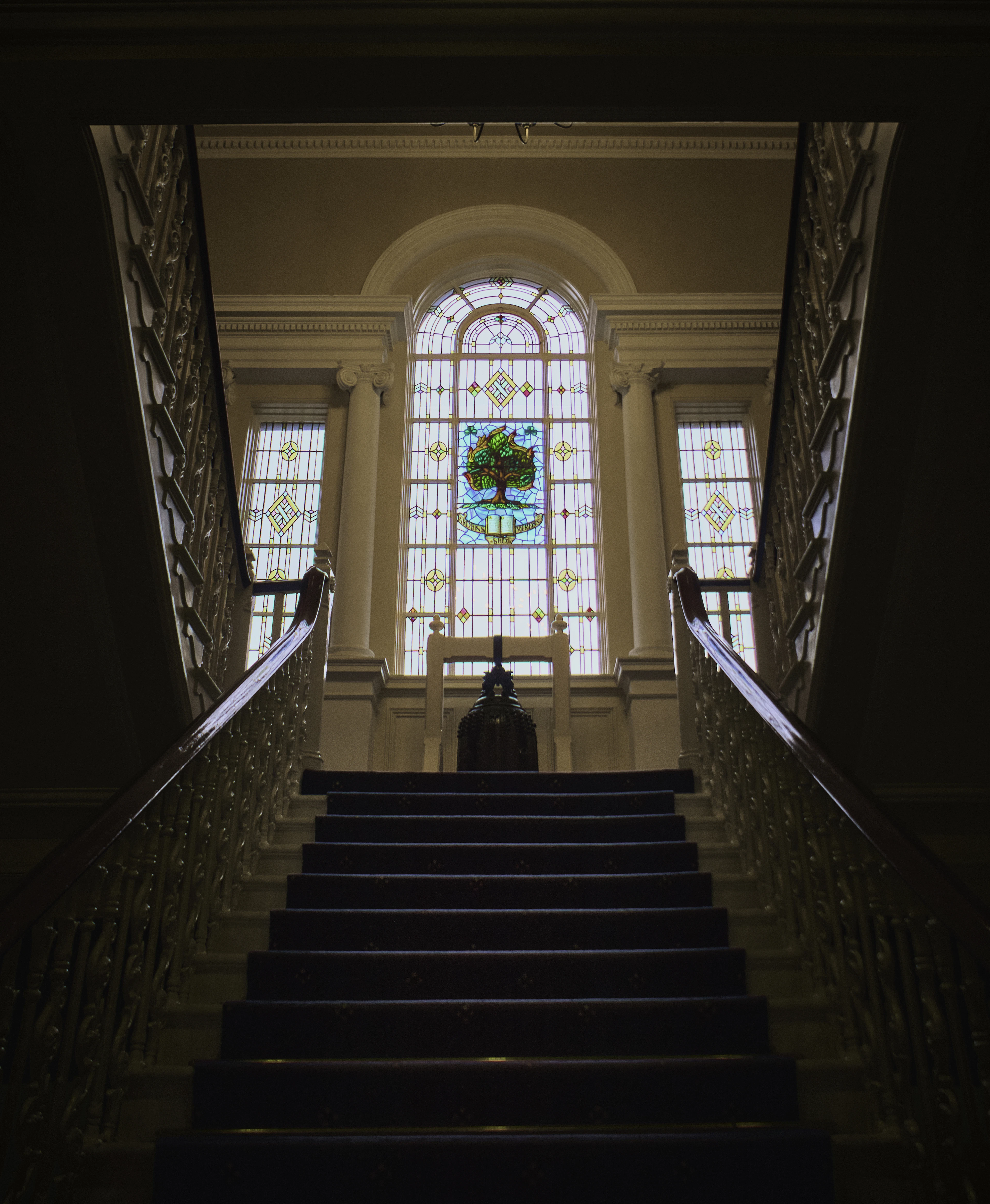 A grand staircase inside a historic Belfast building rising toward a stained-glass tree-of-life window.