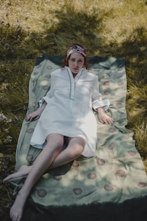 A calm outdoor scene with a woven blanket spread on grass under dappled sunlight.