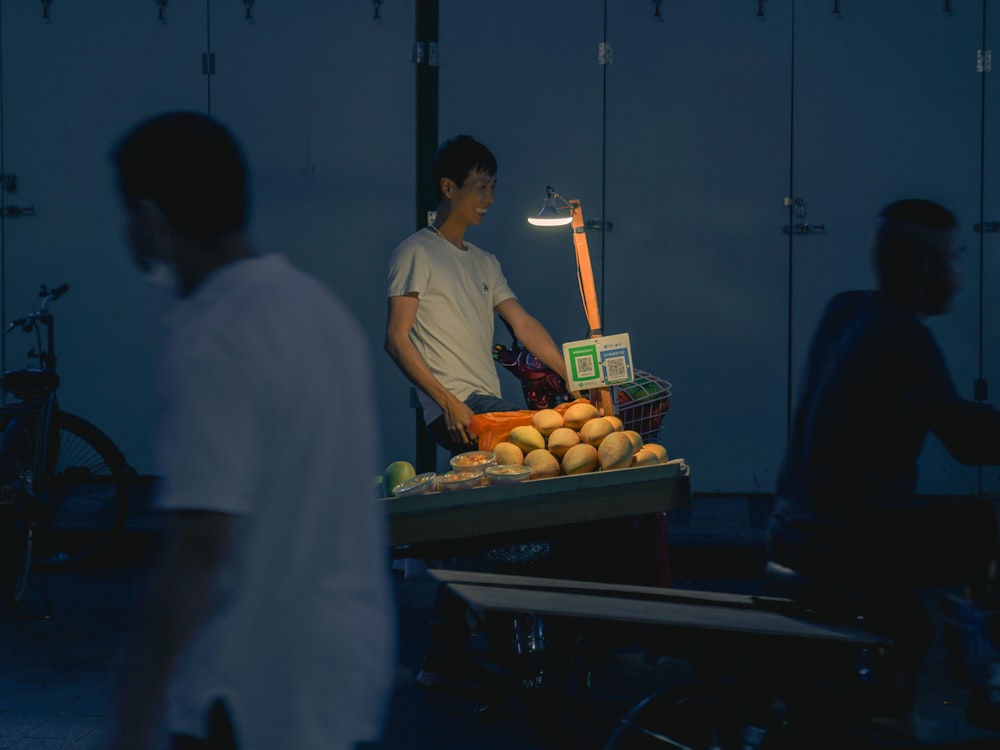 man in white t-shirt standing in front of fruit stand