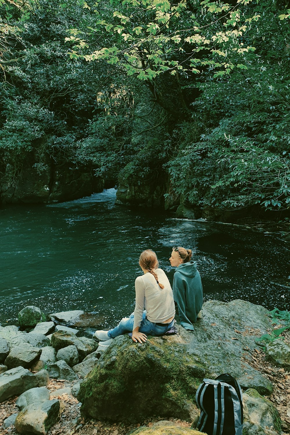 two people sitting on a rock near a river