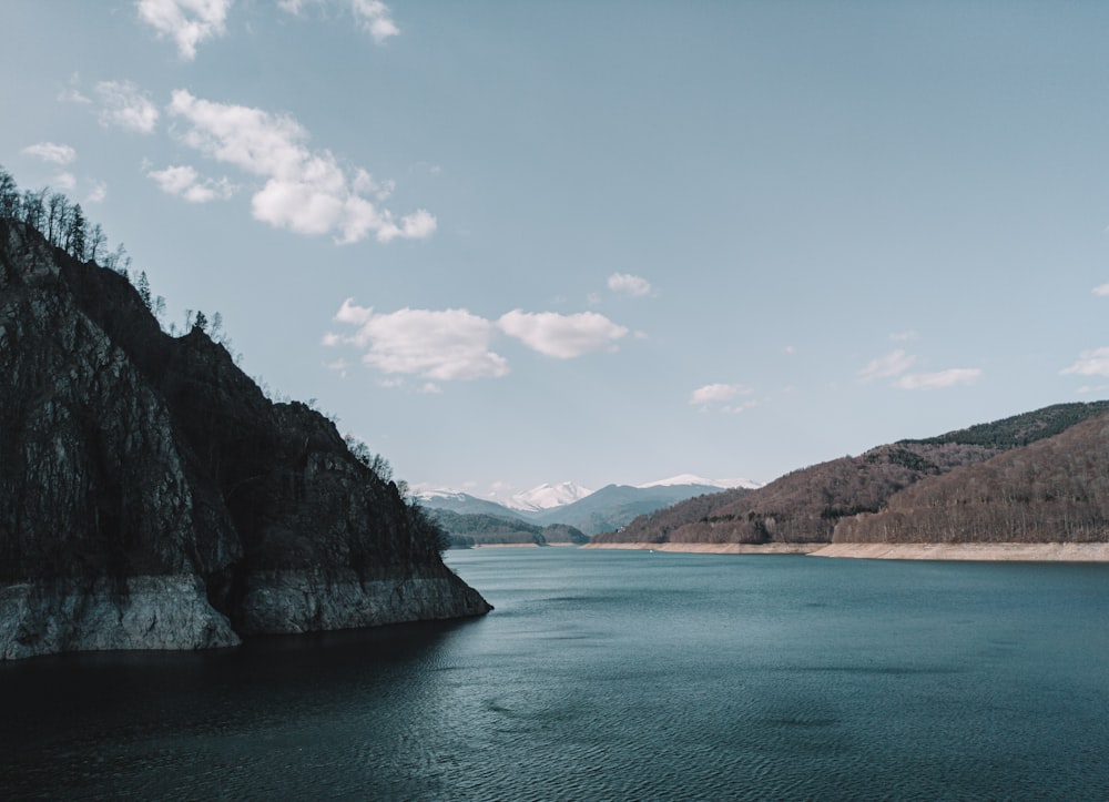 green and brown mountain beside body of water under blue sky and white clouds during daytime