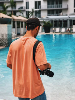 A luxury resort poolside scene at golden hour, with a male travel creator filming content on a sleek camera.
