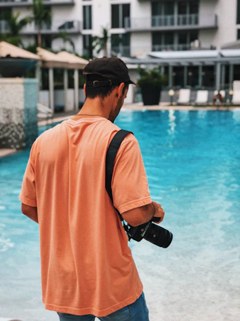 A luxury resort poolside scene at golden hour, with a male travel creator filming content on a sleek camera.