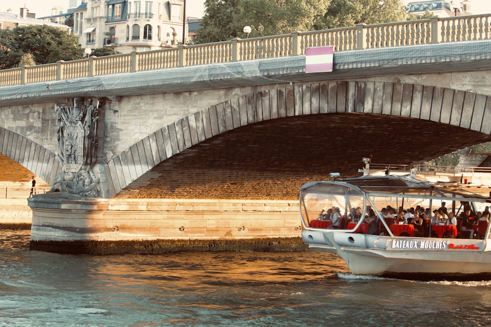 barco branco e marrom na água sob a ponte durante o dia