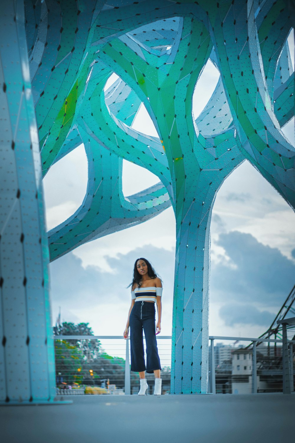 woman in black dress standing near blue metal bridge during daytime