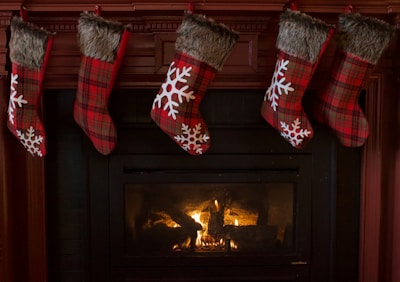 A blue stocking tag featuring a white layered snowflake design, dangling from a stocking above a glowing hearth.