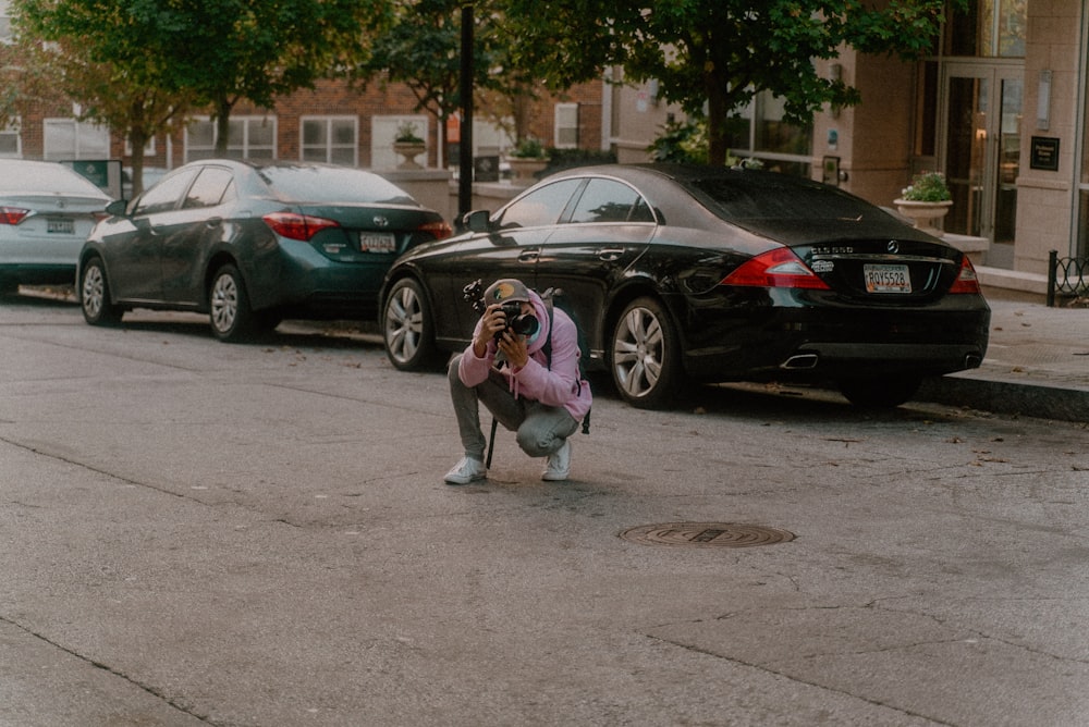 woman in pink jacket and gray pants standing beside black sedan during daytime