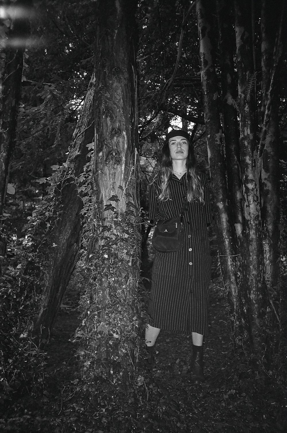 grayscale photo of woman in stripe dress standing in front of tree