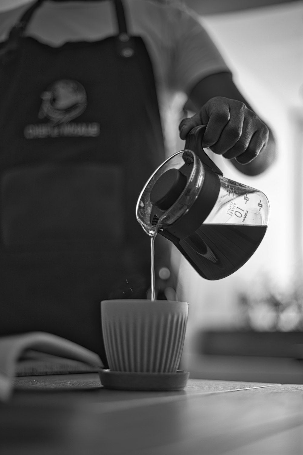 grayscale photo of person pouring coffee on ceramic mug