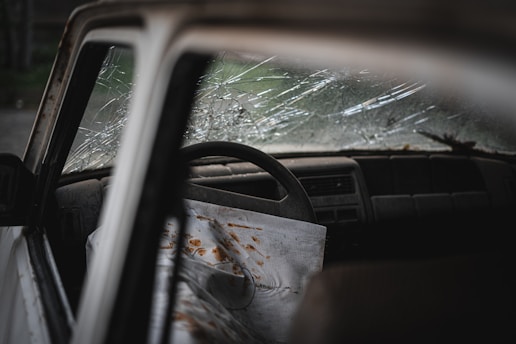 Close-up of hands filling out insurance claim forms next to a cracked windshield.