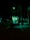 A food truck is parked on a dimly lit street at night, illuminated by a greenish light. The darkness of the surroundings contrasts with the bright interior where a person is visible inside the truck.