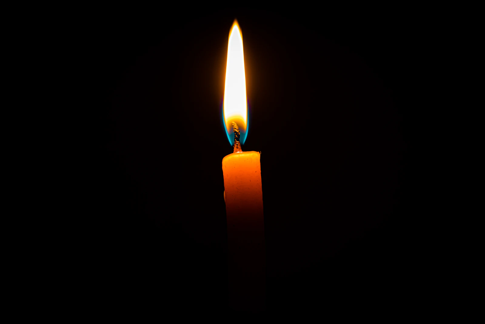 single candle flame glowing in a dark room