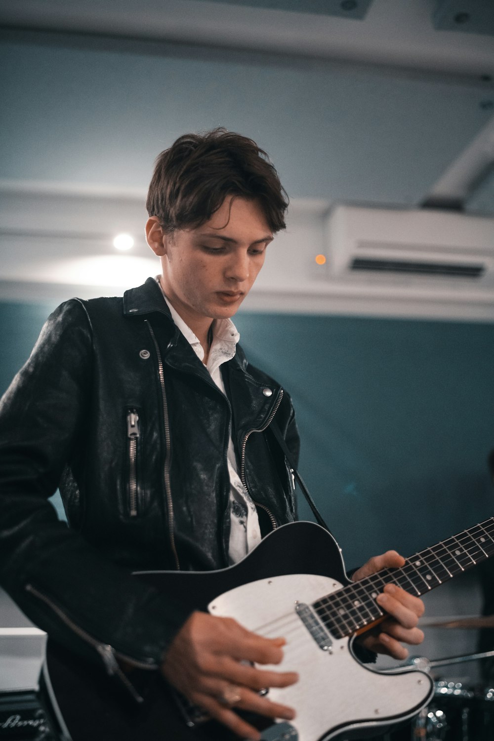 man in black leather jacket holding white acoustic guitar