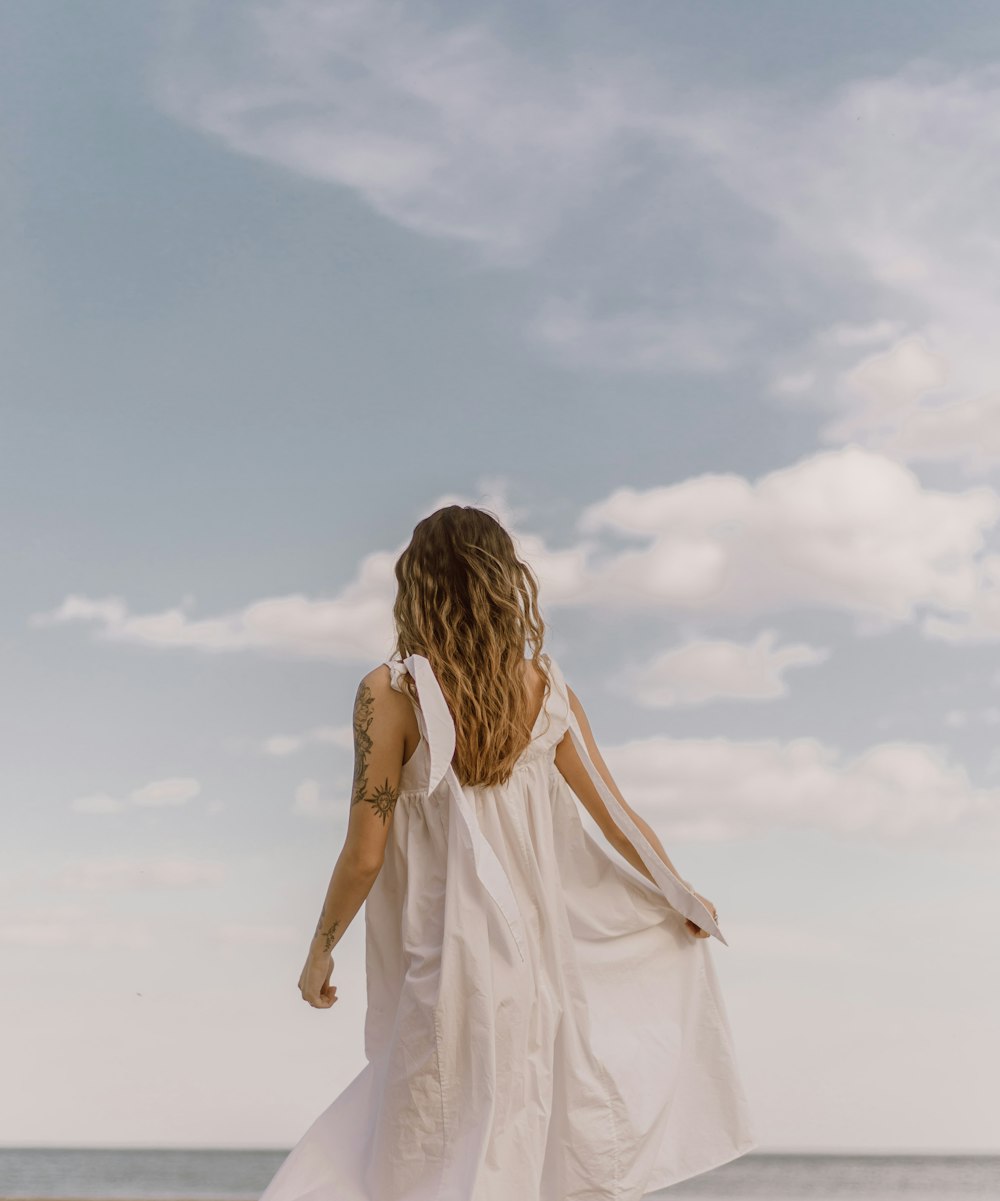 낮에 하얀 모래 위에 서 있는 하얀 드레스를 입은 여자