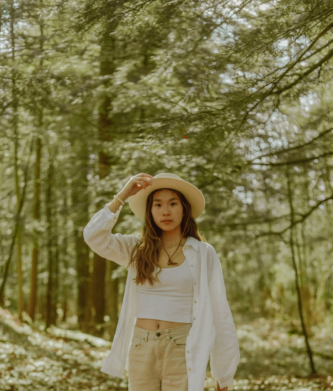 woman in white long sleeve shirt and white hat standing in forest during daytime