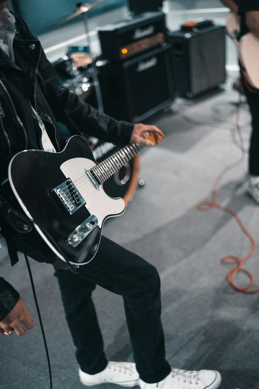 hombre con chaqueta negra tocando guitarra eléctrica blanca