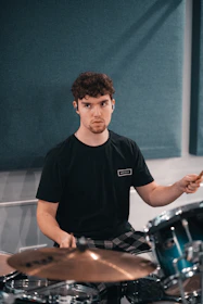 A focused student playing drums energetically in a modern music school room.