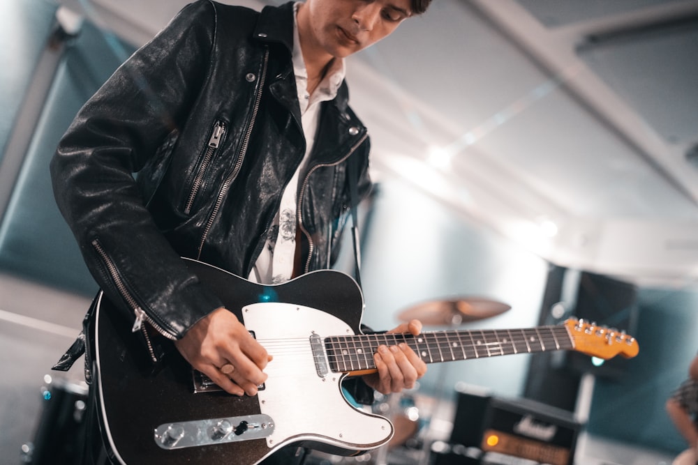man in black leather jacket playing white electric guitar