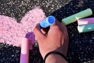 A close-up of a child’s hands holding colorful chalk, drawing on a blackboard.