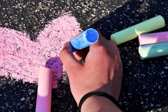 A close-up of a child’s hands holding colorful chalk, drawing on a blackboard.