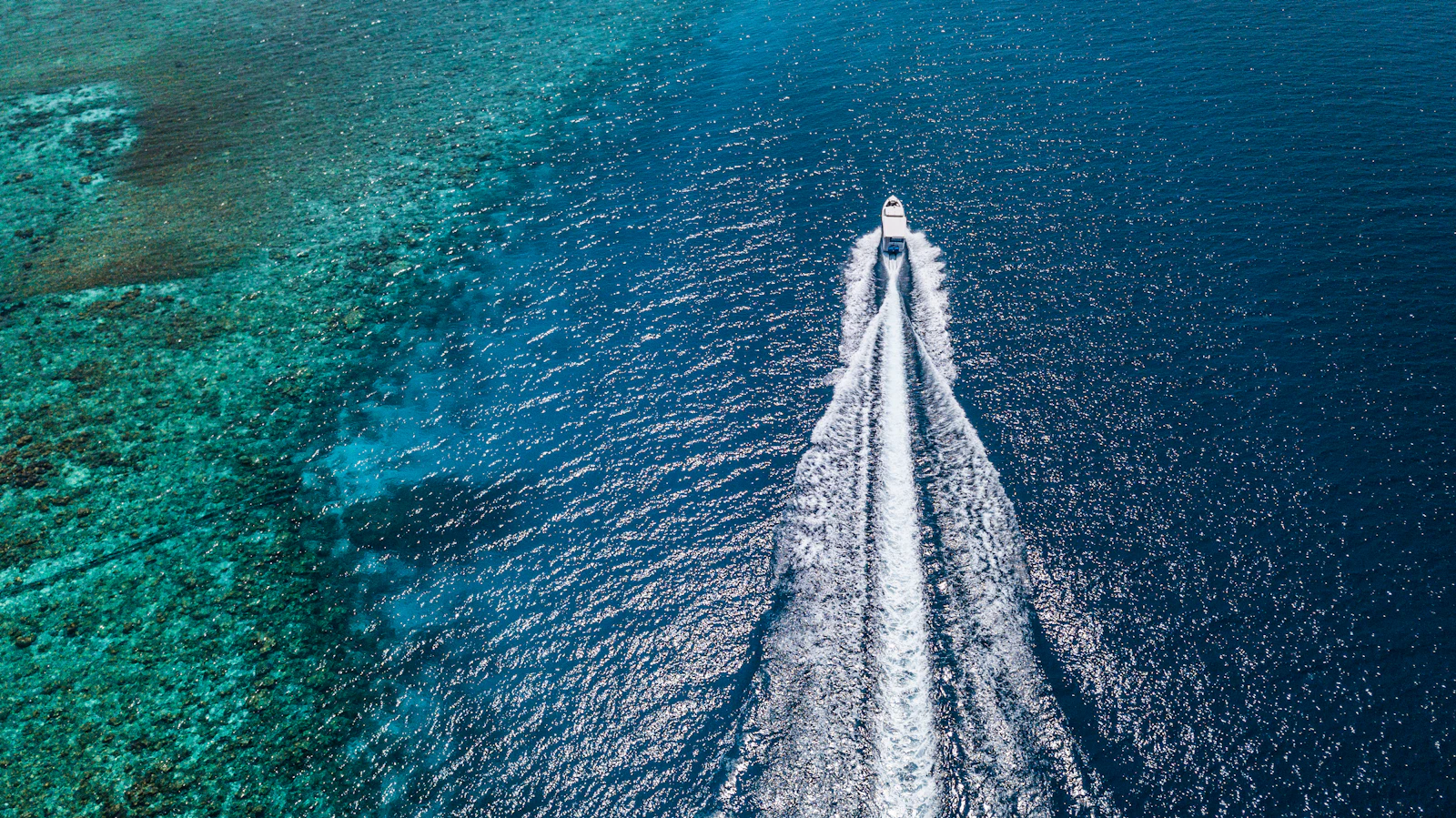 A speedboat leaving a white wake across turquoise water, seen from above