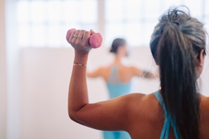 woman in blue tank top holding pink dumbbell