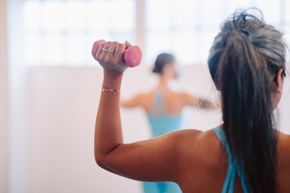 woman in blue tank top holding pink dumbbell