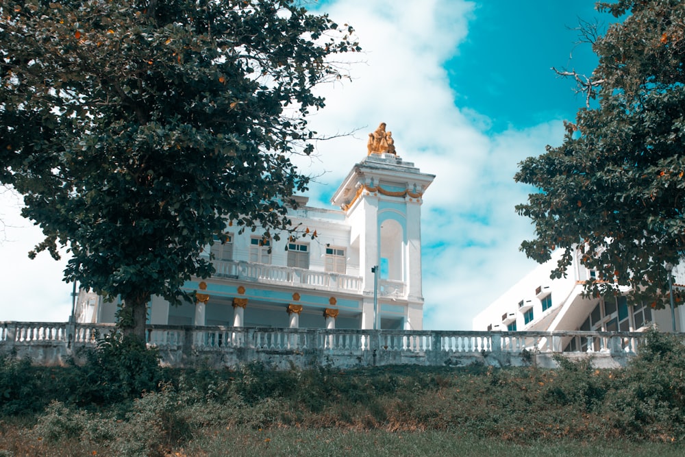 white and yellow concrete building near green trees under blue sky and white clouds during daytime