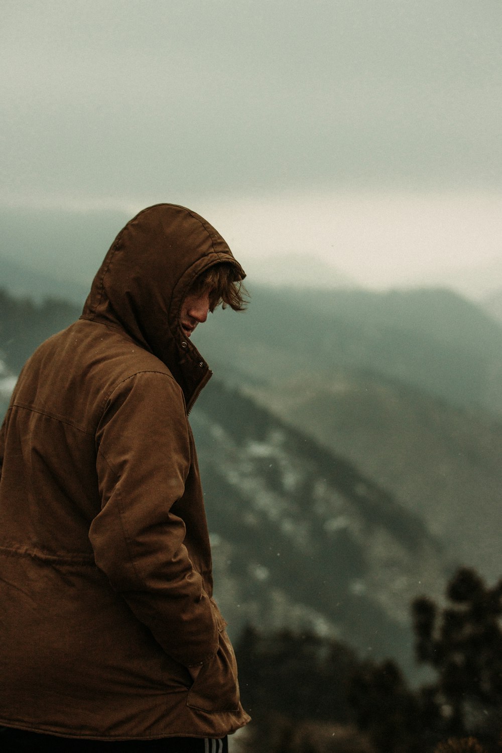 man in brown hoodie standing on snow covered ground during daytime