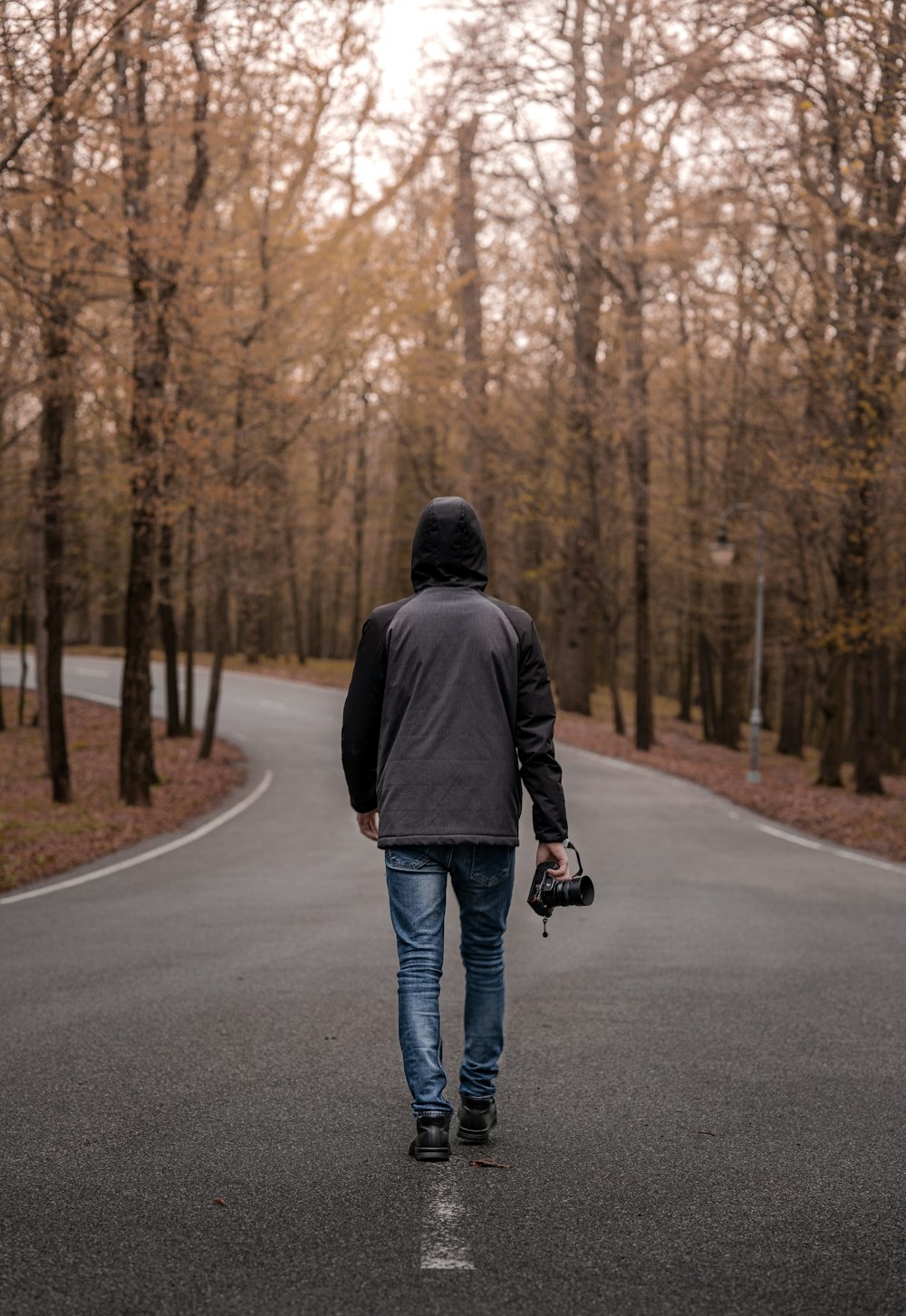 man in black jacket and blue denim jeans walking on road during daytime