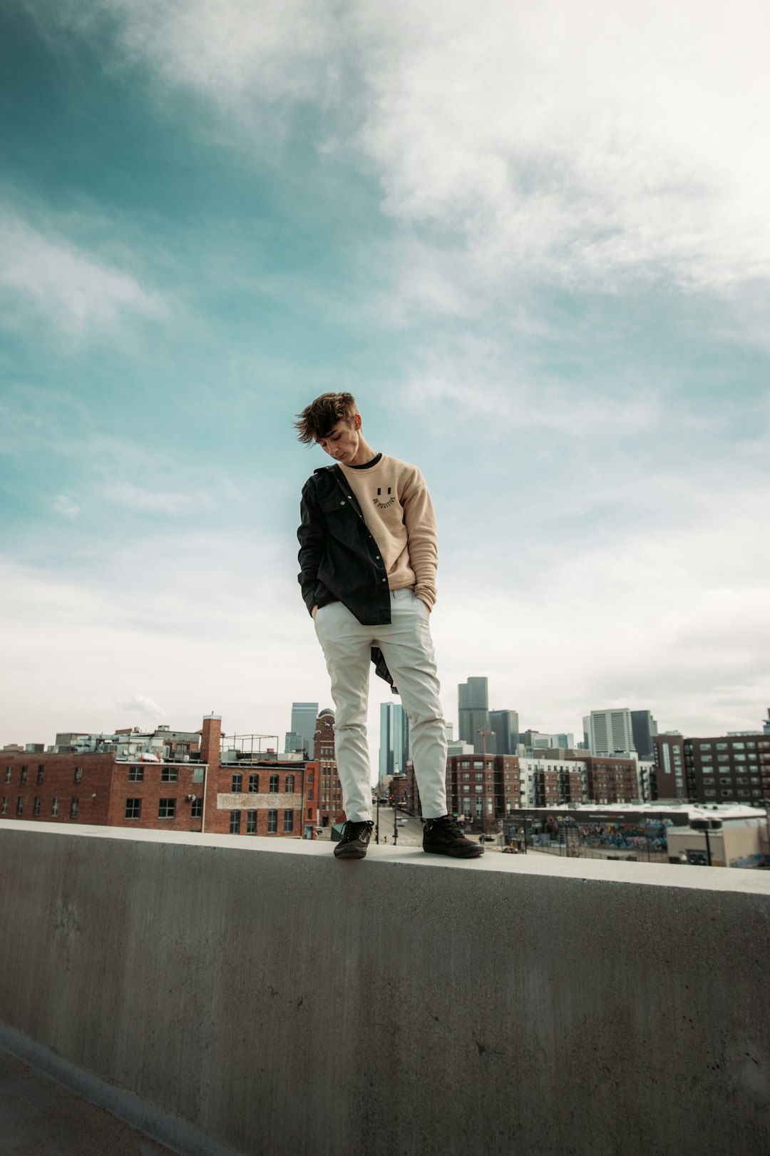 man in black jacket and beige pants standing on gray concrete wall during daytime