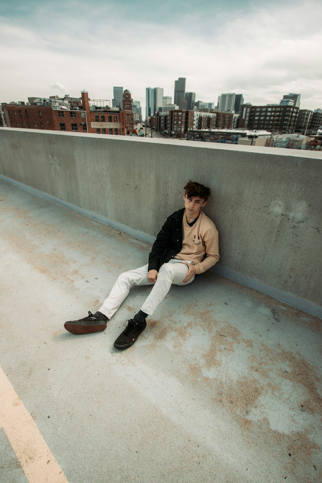 woman in black jacket and white pants sitting on concrete wall