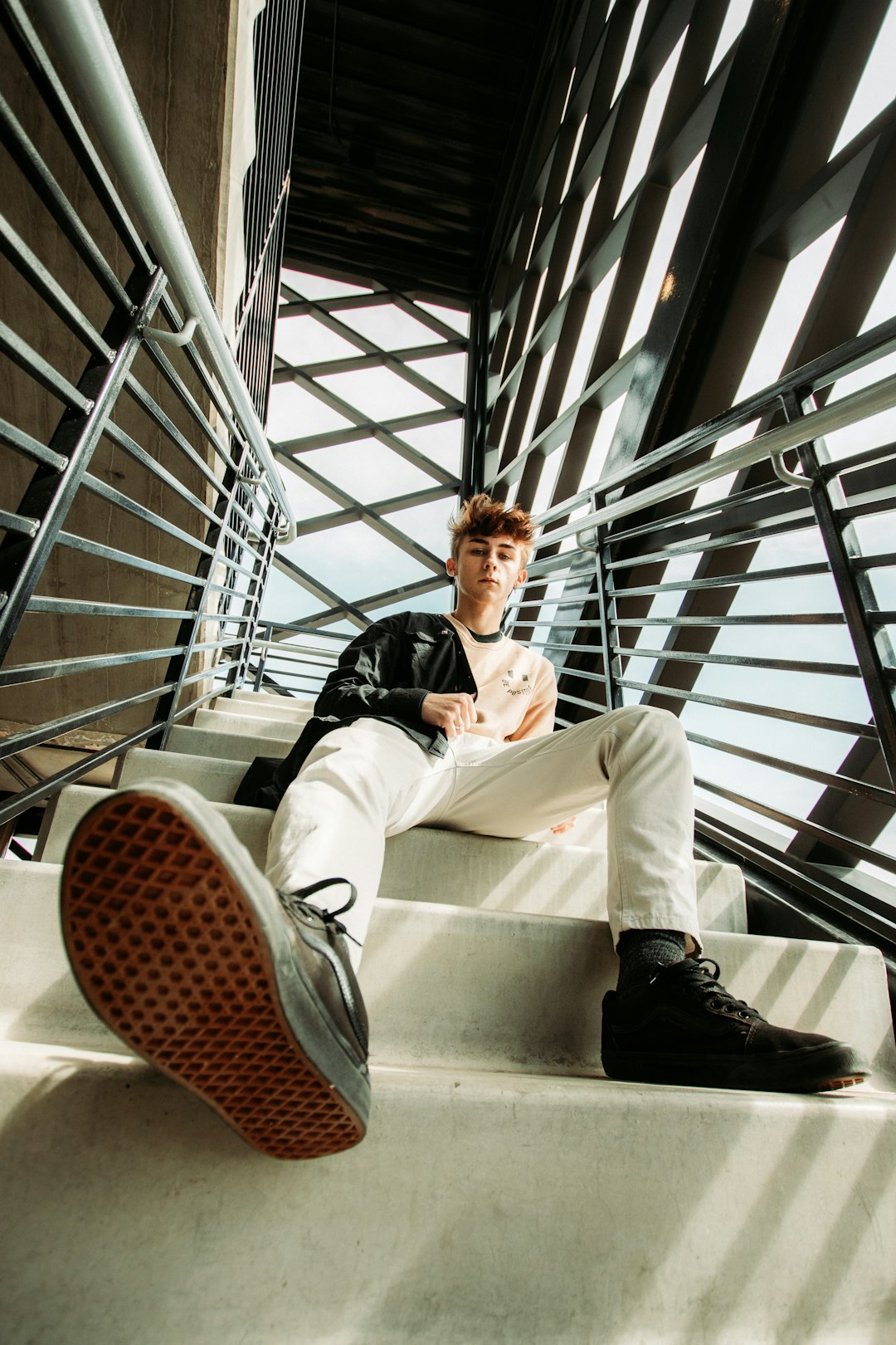 man in black jacket and white pants sitting on white concrete staircase