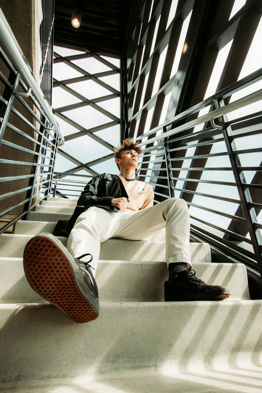 man in black jacket and white pants sitting on white concrete staircase