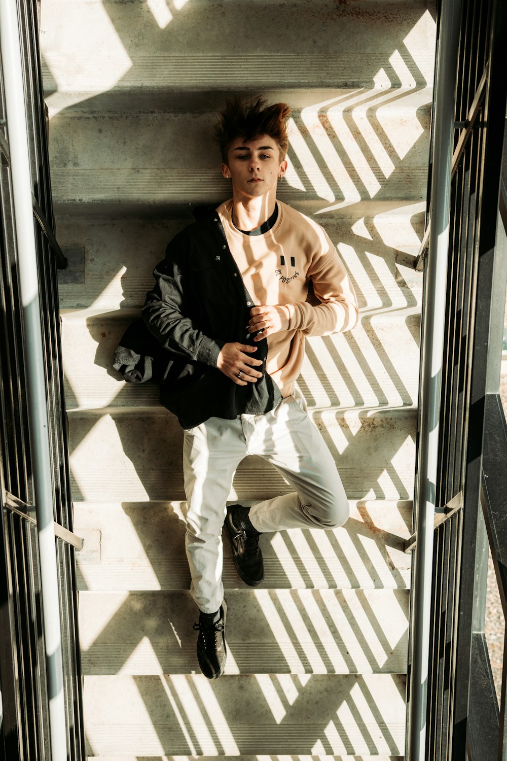 man in black jacket and white pants sitting on white concrete wall